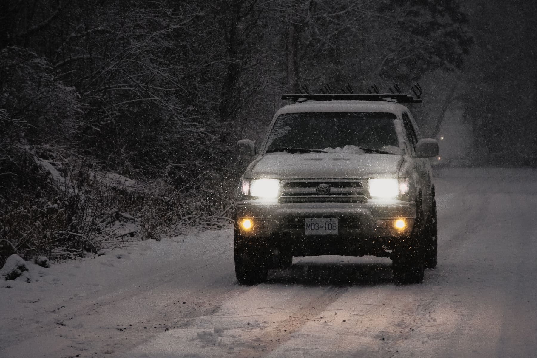 An SUV with headlights on driving through falling snow on a forest road in British Columbia